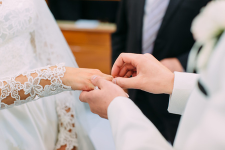 Groom`s hands putting the wedding ring on the finger of the brideの写真素材