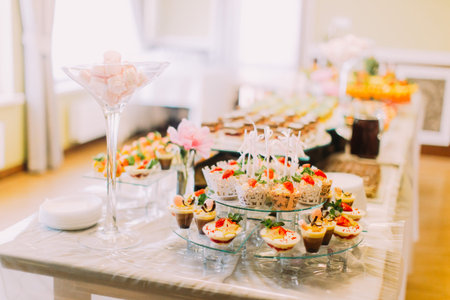 Delicious wedding cupcakes are laying on the dessert stand while the pink marshmallows in the huge...