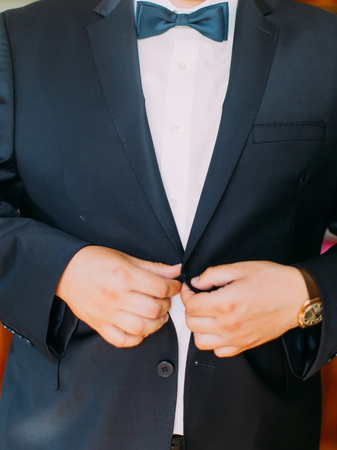 The hands of the groom are buttoning the wedding jacketの写真素材