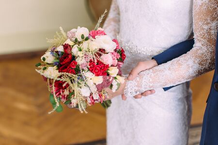 Close-up view of the hands of the bride holding the colouful bouquet of roses and different herbsの写真素材