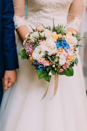 Th vertical close-up view of the wedding bouquet of white, blue and pink flowers in the hands of the brideの写真素材