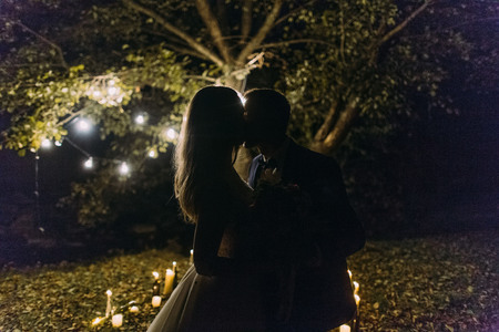 The silhouette of the kissing newlyweds at the background of the lighting candles in the parkの写真素材