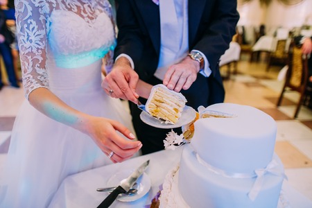 Groom puts the first piece of the wed cake on the plate. Close-up view of the handsの写真素材