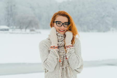 Half-length portrait of the charming red head woman with beautiful smile and glasses in the countryside during the snowfall.の写真素材
