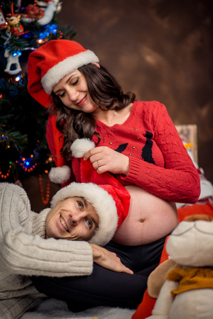 Close-up family portrait of the smiling groom lying on the legs of his pregnant lover while she is playing with his Santa Claus hat.の写真素材