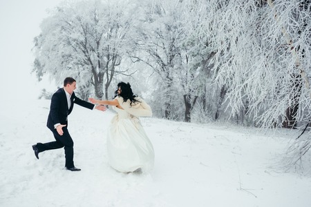 Happy dancing newlywed couple on the snow in the beautiful forest.の写真素材