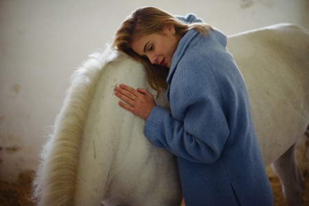 Gorgeous lady in blue coat hugs white horse.の写真素材