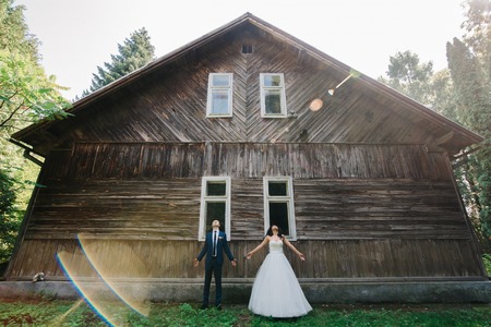 Bride and groom spread their hands standing before old wooden hoの写真素材