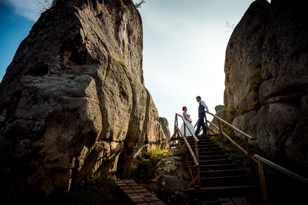 Glamour happy newlywed couple is standing on the wooden stairs between two rocks during the sunset.の写真素材
