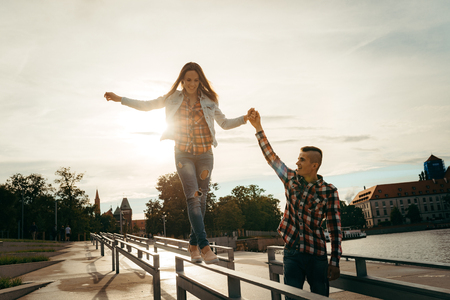Cheerful walk of two lovers holding hands during the sunset near the Ostrow Tumski in Wroclaw, Poland. The girl is walking along the iron fence with the help of her boyfriend hand.の写真素材