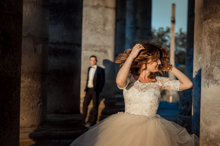 Emotional portrait of the beautiful attractive bride shaking and touching her ginger curly hair at the blurred background of the doom near old castle during the sunset.の写真素材