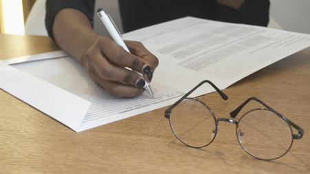 African girl at the reception is writing something in the from. No face. Female hands. Eyeglasses in...