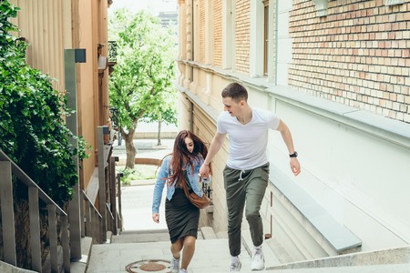 Close-up portrait of the young pretty loving couple holding hands while going up the stairs in the narrow Budapest street in Hungary.の写真素材