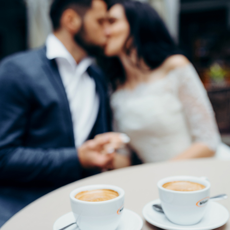 Close-up view of the two cups of coffee at the blurred background of the kissing newlyweds.の写真素材