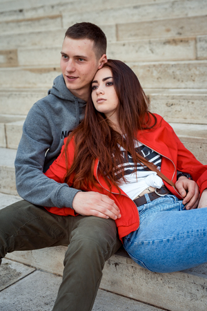 Close-up portrait of the charming young couple in love holding hands and sitting on the stairs of the old historic building in Budapest, Hungary. The red head girl is leaning on her lover.の写真素材