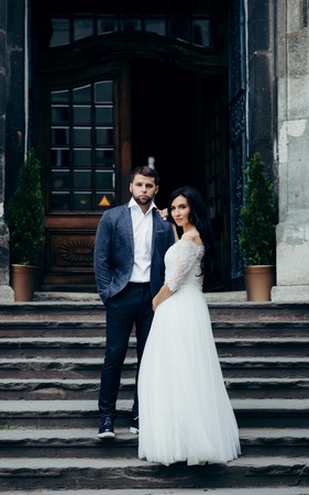 Full-length wedding shot of the beautiful young newlywed couple posing on the stairs of the old church.の写真素材