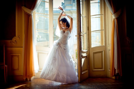 Full-length view of the young attractive charming bride in the gorgeous wedding dress posing near the window of the old rich palace.の写真素材