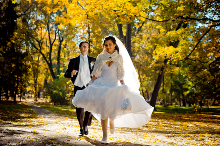 Emotional wedding portrait of the handsome groom running after the beautiful gorgeous bride along the autumn park.の写真素材