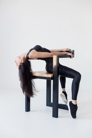 Portrait of the sportive woman in sportwear stretching her back while sitting on the chair at the white background.の写真素材