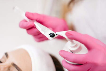 Skin Care and Cosmetics Concept. The beautician is putting the special black cream from bottle on the brush. Getting ready to laser and ultrasound face treatment.の写真素材