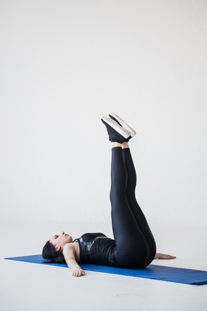 Full-length view of the muscular fitness trainer lying on the yoga mat and raising legs up.の写真素材