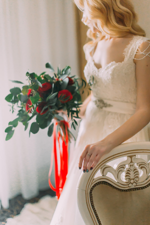 Beautiful bride with bouquet of roses standing near the windowの写真素材