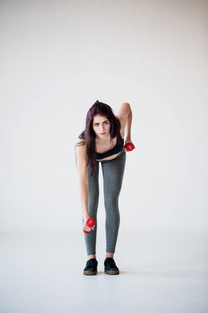 Serious sportwoman is doing hand exercises with dumbbells in the studio. Full-length front view.