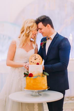 Beautiful blond bride and groom cut the wedding cake togetherの写真素材