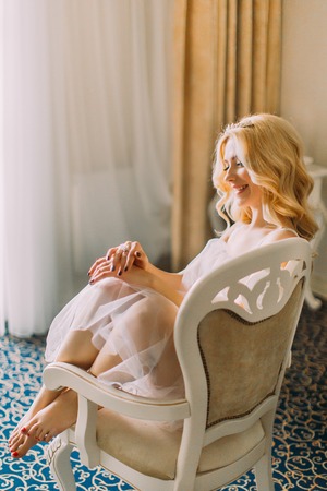 Charming blond bride sitting on armchair and smiling. Luxurious apartments  backgroundの写真素材
