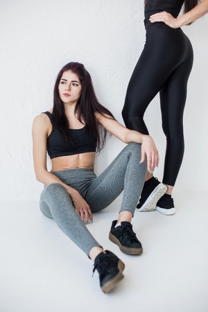 The young charming athletic brunette in sportsuits is sitting on the white floor at the background of the legs of her friend.の写真素材