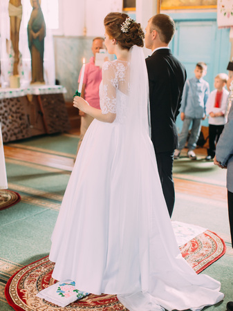 Back view of the newlywed couple standing on the ceremonial embroidered towel in the church.の写真素材