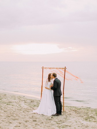 The kissing newlyweds during the wedding ceremony on the beach at the background of the sunset.の写真素材
