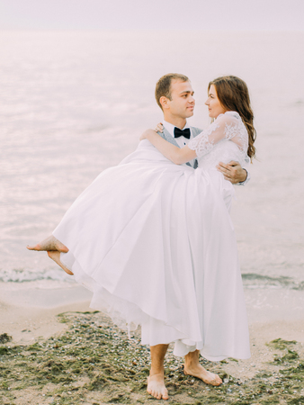 The lovely view of the groom holding the bride in his arms at the background of the sea.の写真素材