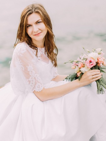 The close-up portrait of the sitting bride and holding the wedding bouquet consisted of the colourful roses at the background of the sea.の写真素材