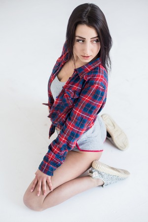 Above view of the young attractive brunette with natural make-up in short shorts and cell shirt sitting on the white floor and looking away.の写真素材