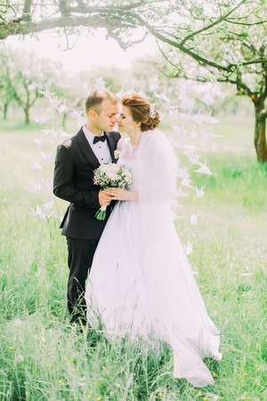 The newlyweds are standing head-to-head in the front of the paper swans hanging on the tree during the spring.の写真素材