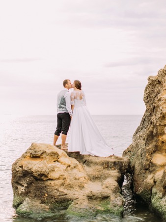 The kissing newlyweds while standing on the cliff among the sea. The back view.の写真素材
