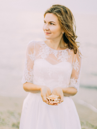 The bride is looking at the right side while holding the shell at the background of the sea.の写真素材