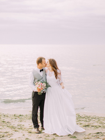 The full-length view of the newlyweds kissing at the background of the sea.の写真素材
