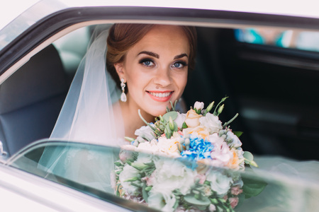 Portrait of the happy smiling bride with the wedding bouquet sitting in the car.の写真素材