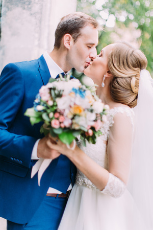 Side view of the kissing newlyweds holding the wedding bouquet.の写真素材