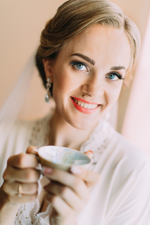 The smiling bride is holding the cup of tea. The close-up portrait.の写真素材