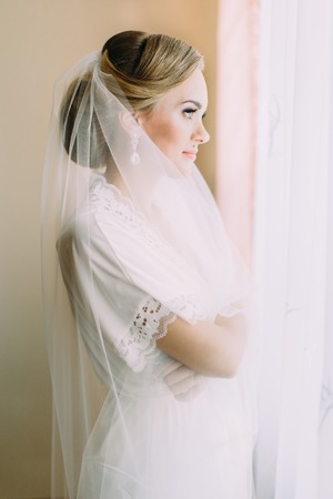 The beautiful bride with veil is looking through the window.の写真素材