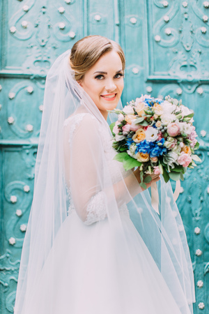 Close-up portrait of the smiling bride holding the wedding bouquet at the background of the blue door.の写真素材