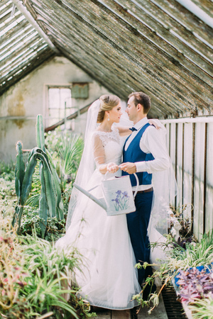 Full-length view of the newlyweds holding the watering can in the greenhouse.の写真素材