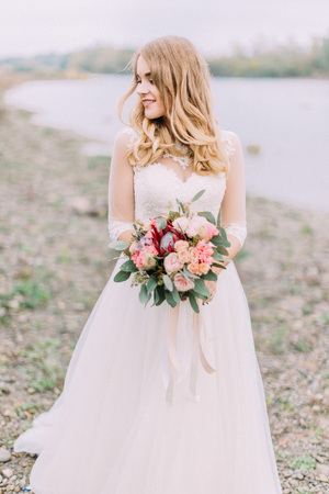The bride with the wedding bouquet is looking aside at the background of the beach.の写真素材