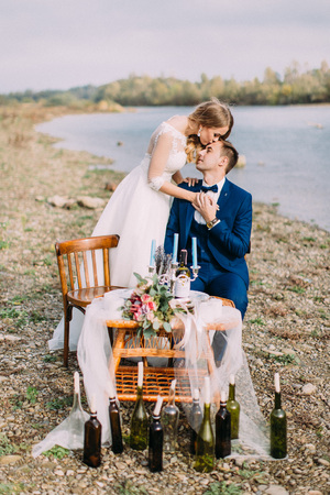 Beautiful bride is kissing the sitting groom in the forehead. Beach location.の写真素材
