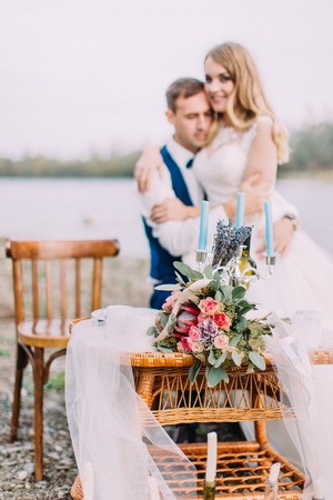 Lovely wedding table set with bouquet of flowers at the blurred background of the newlyweds.の写真素材