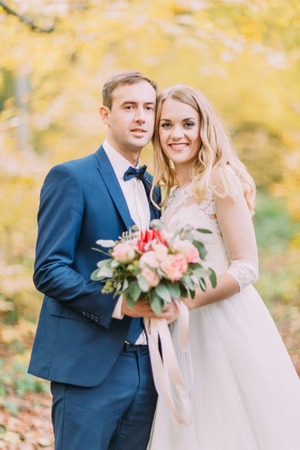 Happy newlywed couple holding the wedding bouquet at the blurred background of the autumn forest.の写真素材