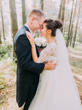 Half-length romantic portrait of the cheerful hugging newlyweds standing head-to-head in the forest.の写真素材